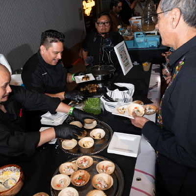 Chefs in black uniforms plating signature bites for guests at a culinary station.