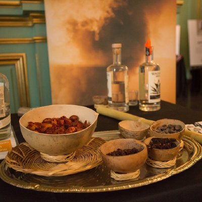 Still life of artisanal Mexican products featuring mezcal bottles and ingredients in traditional wooden bowls.